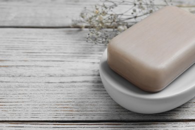 Photo of Dish with soap bar on wooden table, closeup. Space for text