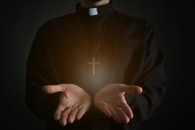 Image of Priest reaching out his hands with holy light on dark background, closeup