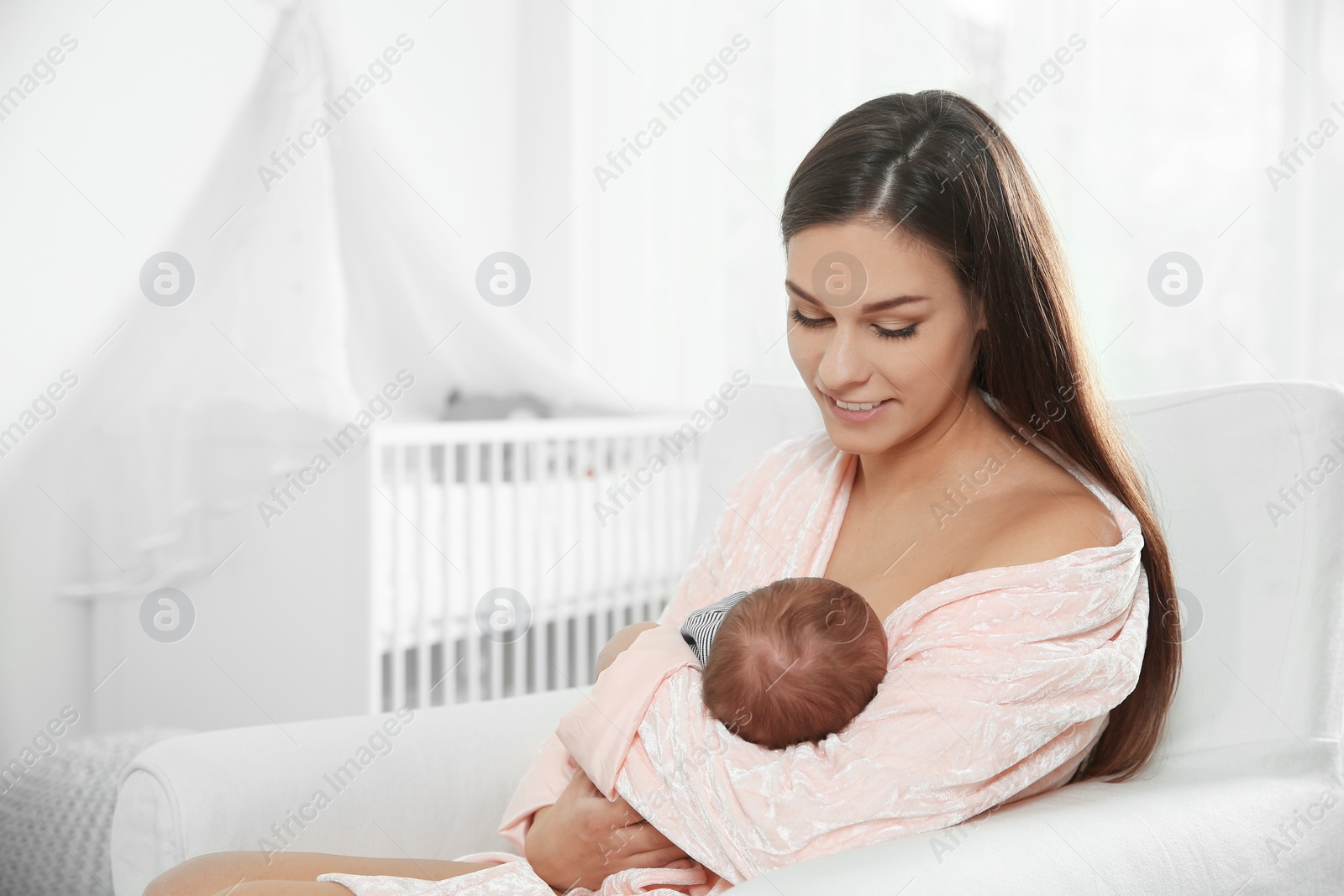 Photo of Young woman breastfeeding her baby in nursery. Space for text