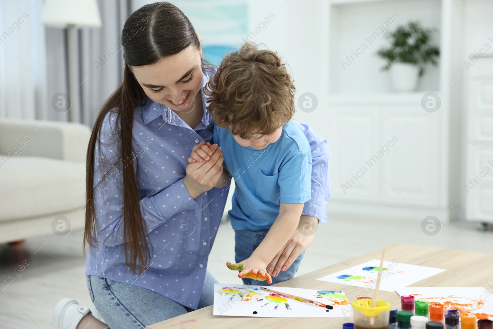 Photo of Mother and her little son painting with palms at home