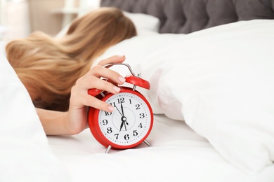 Photo of Woman turning off alarm clock in bedroom