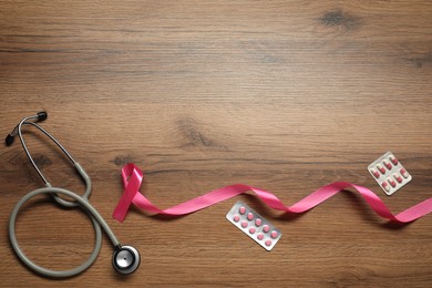 Photo of Breast cancer awareness. Pink ribbon, stethoscope and pills on wooden table, flat lay. Space for text