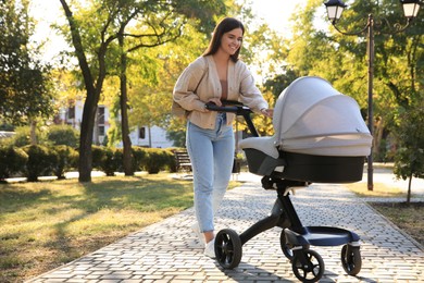 Young mother walking with her baby in stroller at park on sunny day