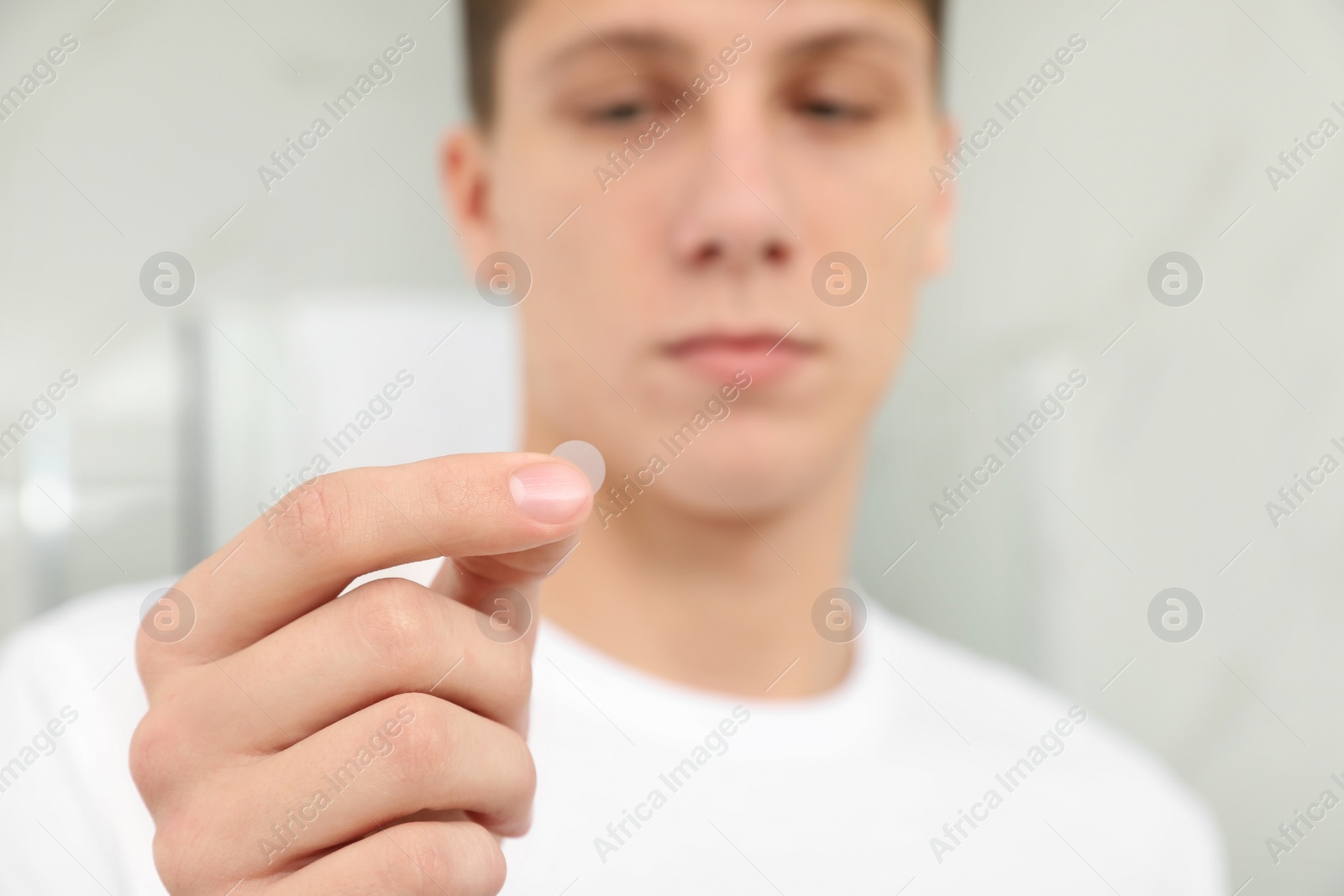 Photo of Teen guy using acne healing patch indoors, focus on hand