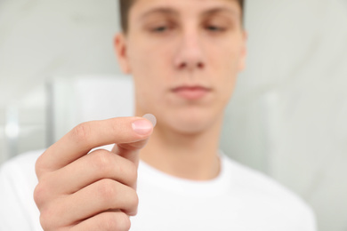 Photo of Teen guy using acne healing patch indoors, focus on hand