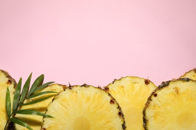 Photo of Slices of tasty ripe pineapple and green leaves on pink background, flat lay. Space for text