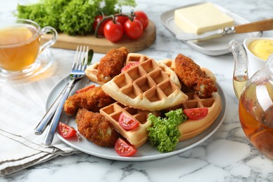 Photo of Tasty Belgian waffles served with fried chicken, tomatoes, lettuce and tea on white marble table