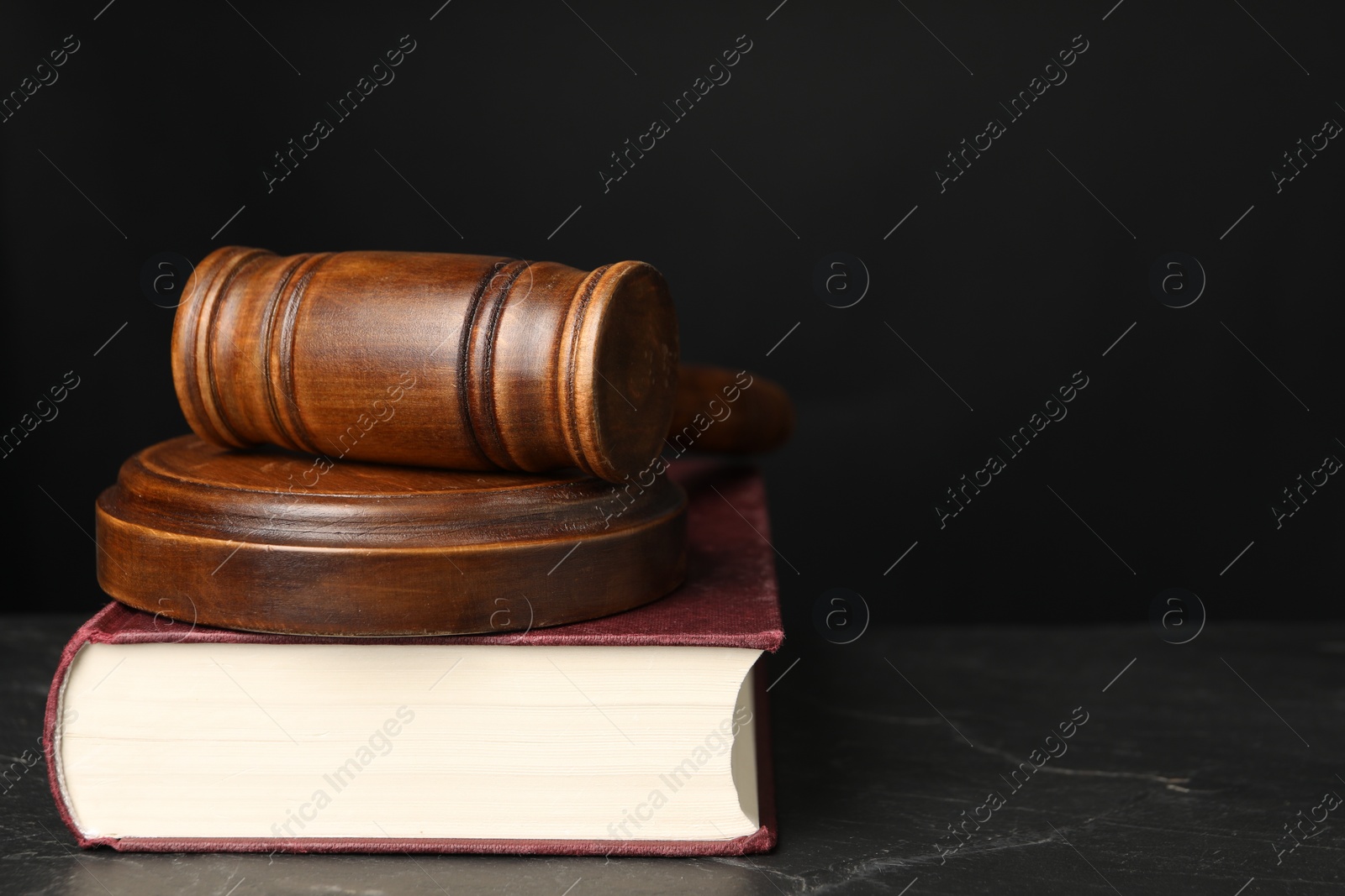 Photo of Wooden gavel, sound block and book on dark textured table, closeup. Space for text