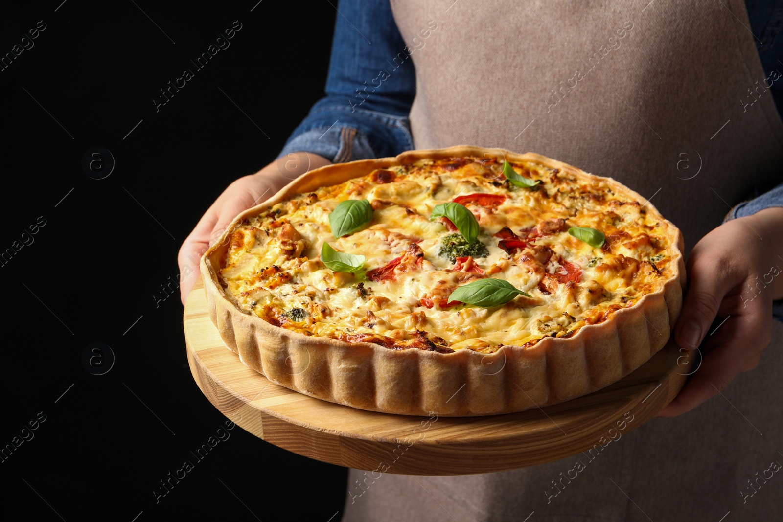 Photo of Woman holding board with tasty quiche on black background, closeup