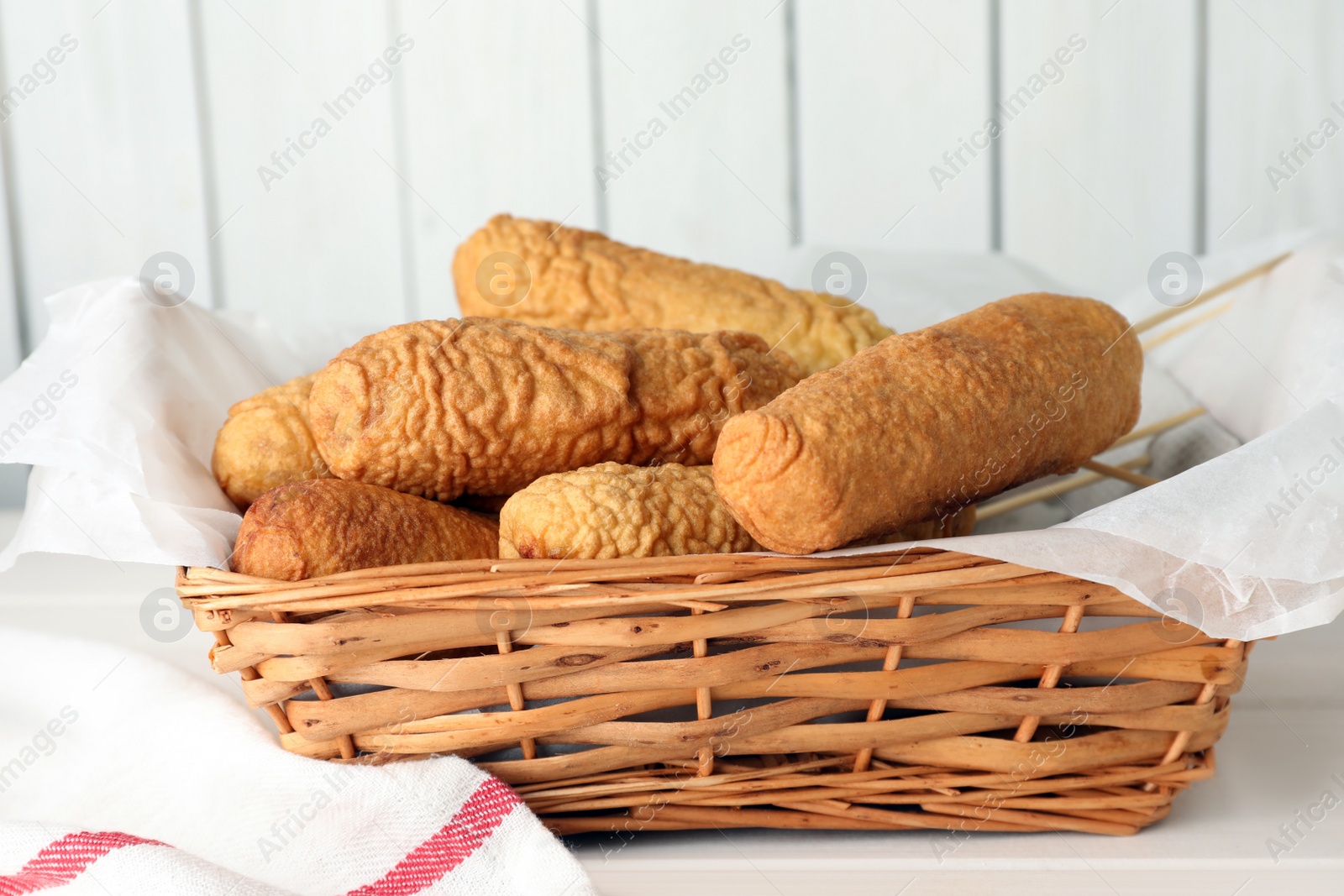 Photo of Delicious deep fried corn dogs in basket on white wooden table