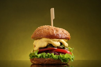 Photo of Delicious vegetarian burger on mirror surface against olive background