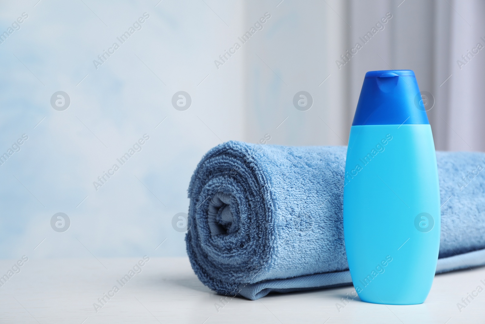 Photo of Bottle with shampoo and rolled bath towel on table, space for text