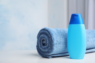 Photo of Bottle with shampoo and rolled bath towel on table, space for text