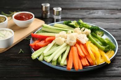 Photo of Plate with celery sticks, other vegetables and different dip sauces on dark wooden table