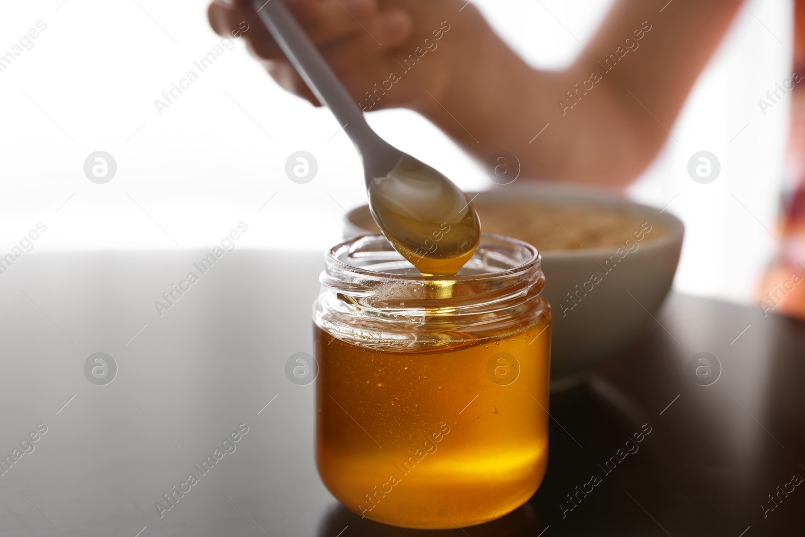 Photo of Woman with honey and spoon at black table, closeup