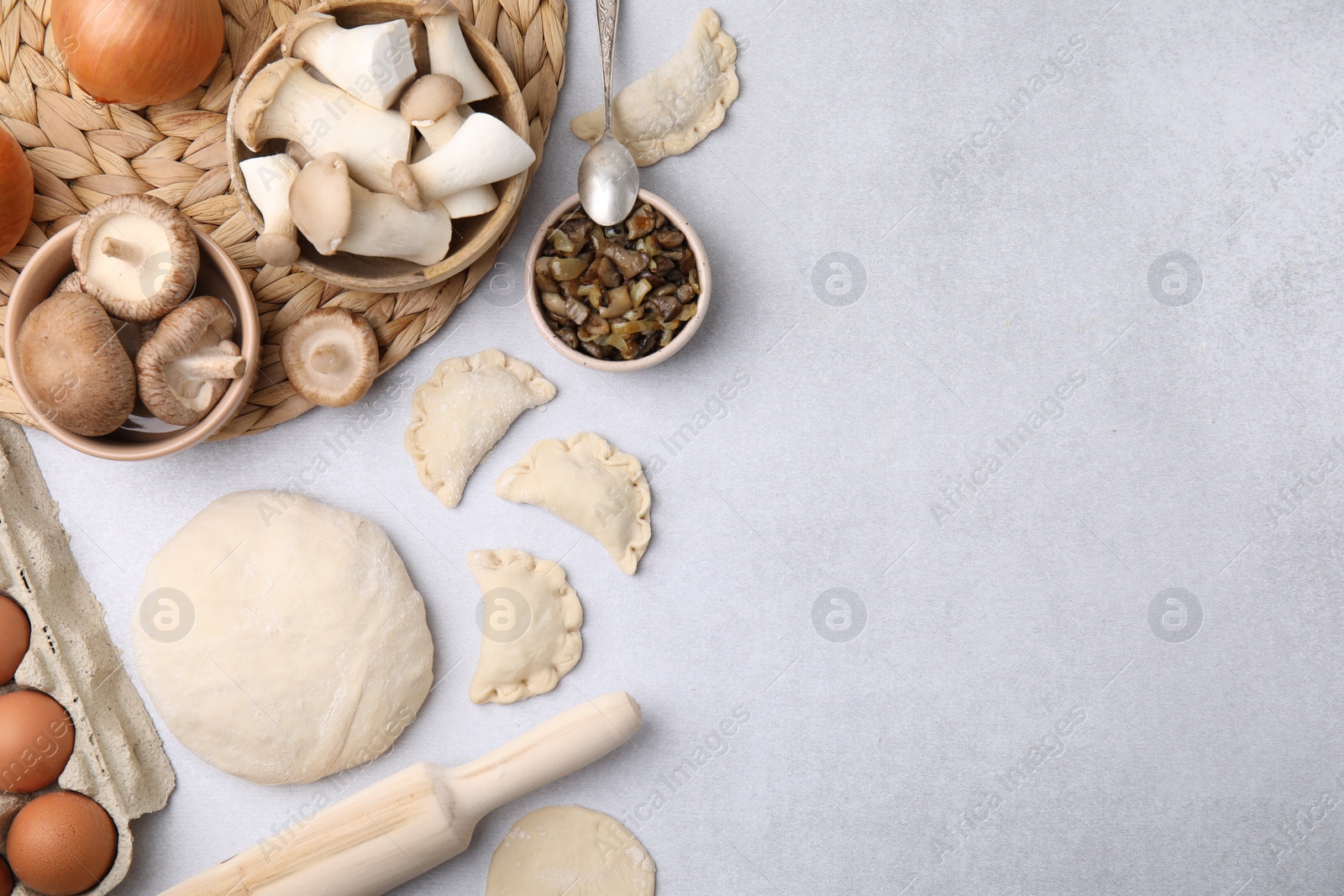 Photo of Process of making dumplings (varenyky) with mushrooms. Raw dough and ingredients on white table, flat lay. Space for text