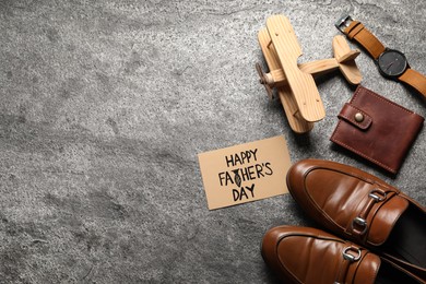 Photo of Card with phrase Happy Father's Day, shoes, toy plane and men accessories on grey background, flat lay. Space for text