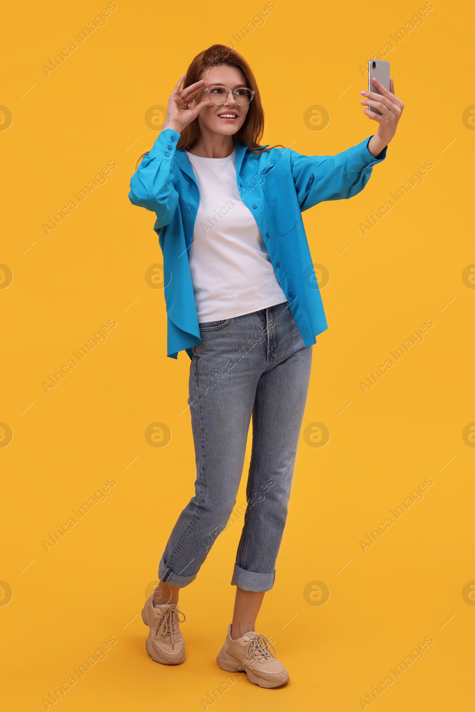 Photo of Beautiful woman in eyeglasses taking selfie on orange background