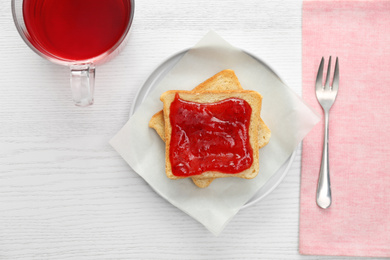 Tasty toast with jam and raspberry tea on white wooden table, flat lay. Delicious morning meal