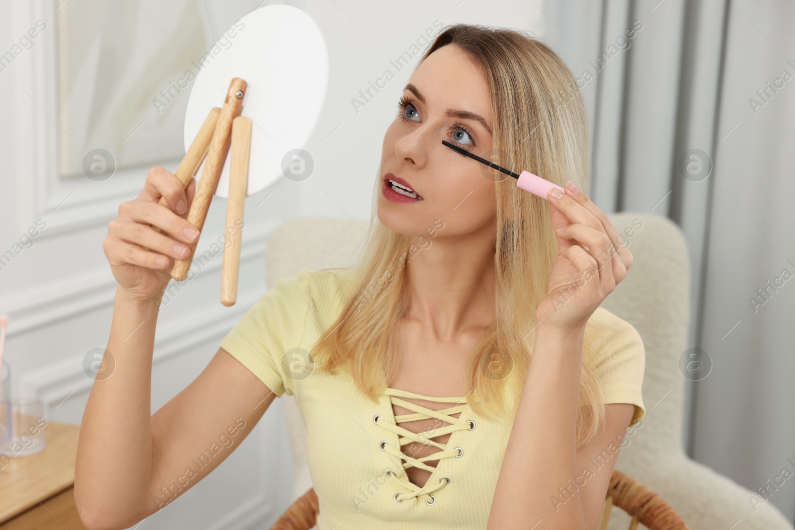 Photo of Beautiful woman with mirror applying mascara at home