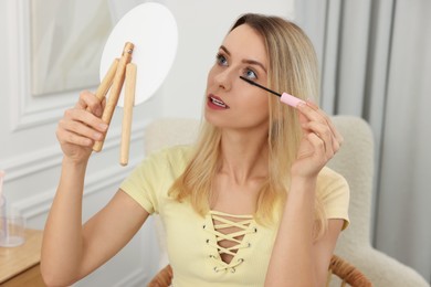 Photo of Beautiful woman with mirror applying mascara at home