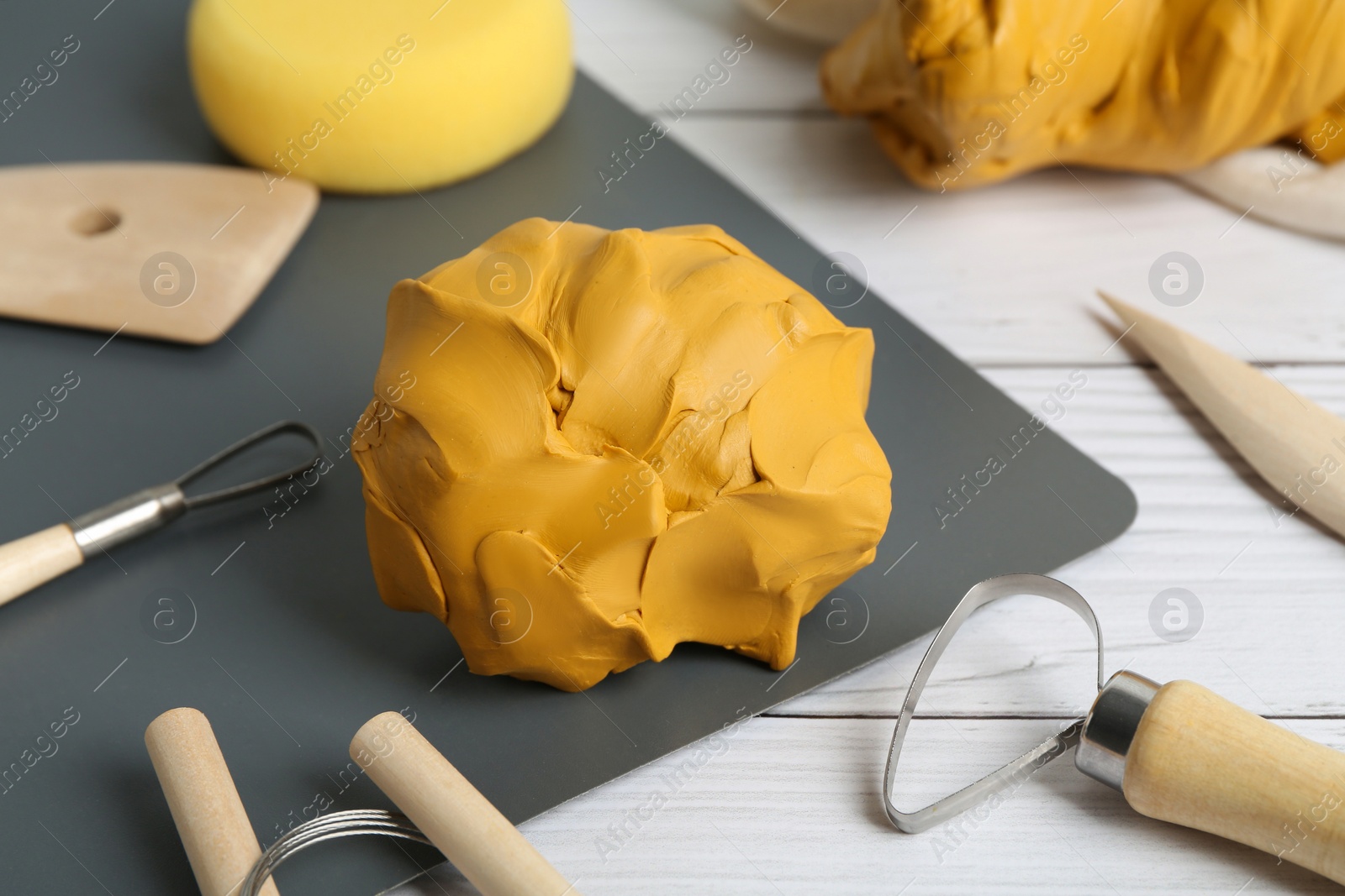 Photo of Clay and set of modeling tools on white wooden table, closeup