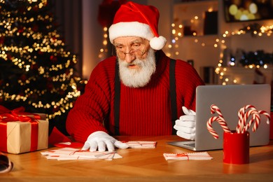 Santa Claus at his workplace. Letters and laptop on table in room decorated for Christmas
