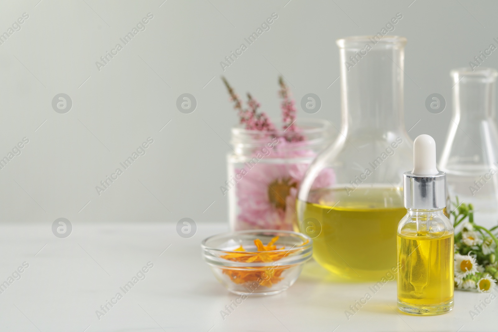 Photo of Cosmetic oil, laboratory dishware and flowers on white table, space for text
