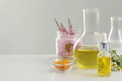 Photo of Cosmetic oil, laboratory dishware and flowers on white table, space for text