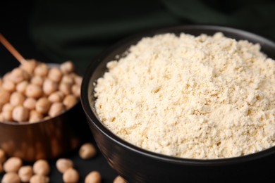 Photo of Chickpea flour in bowl and seeds on black table, closeup