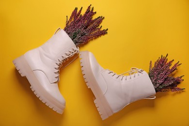 Photo of Pair of stylish leather shoes with heather flowers on yellow background, flat lay