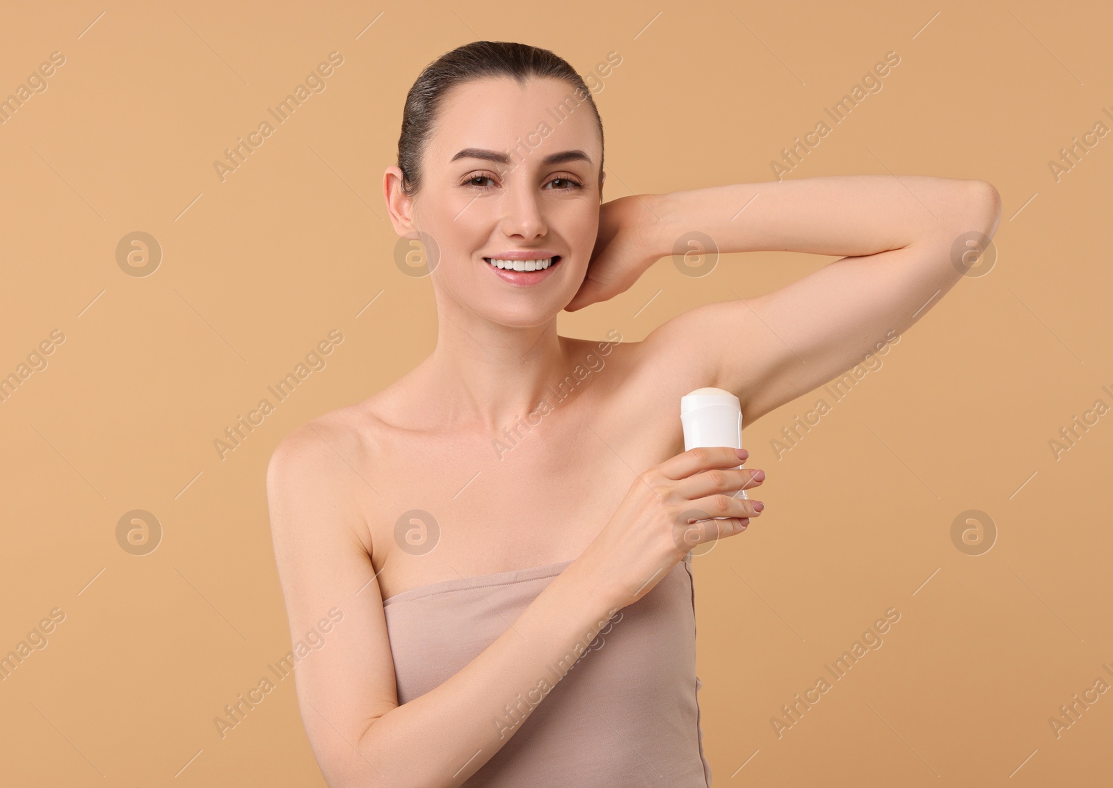 Photo of Beautiful woman applying deodorant on beige background