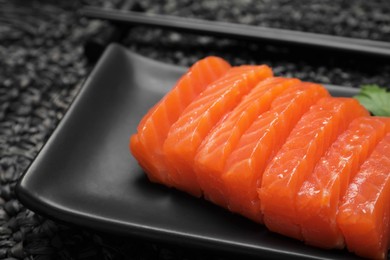 Photo of Plate of tasty salmon slices on black wicker mat, closeup. Delicious sashimi dish