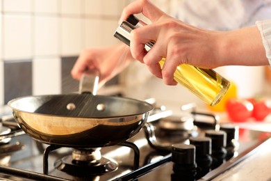 Photo of Vegetable fats. Woman sprinkling oil into frying pan on stove in kitchen, closeup