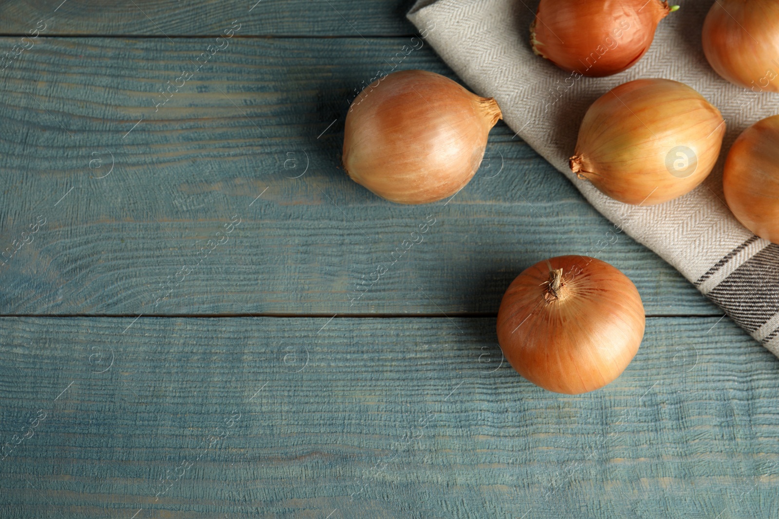 Photo of Flat lay composition with ripe onions and fabric on blue wooden table, space for text