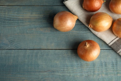 Flat lay composition with ripe onions and fabric on blue wooden table, space for text