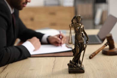 Photo of Lawyer working at table in office, focus on statue of Lady Justice