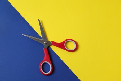 Red scissors and blue paper on yellow background, top view. Space for text