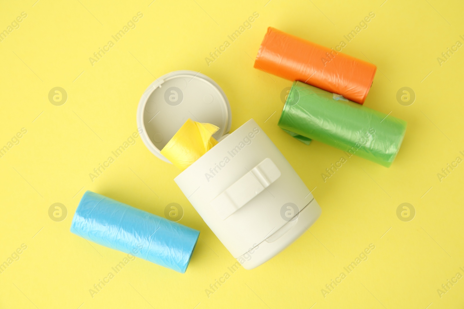 Photo of Dog waste bags and dispenser on yellow background, flat lay