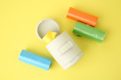 Dog waste bags and dispenser on yellow background, flat lay