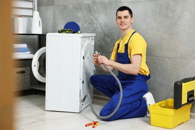 Photo of Young plumber examining drain hose of washing machine in bathroom