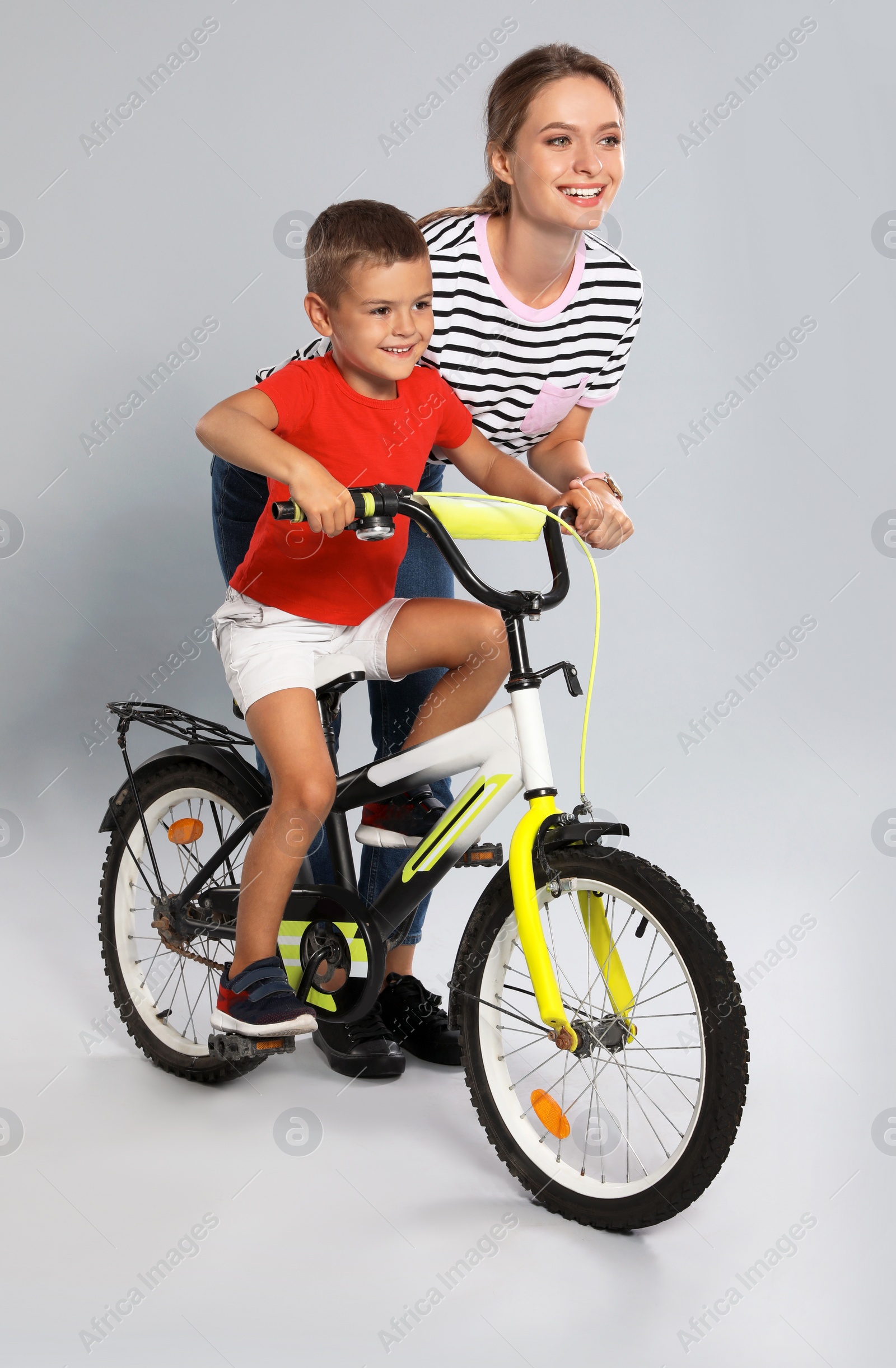 Photo of Young mother teaching son to ride bicycle on grey background