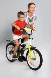 Photo of Young mother teaching son to ride bicycle on grey background