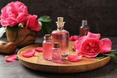 Wooden tray with bottles of rose essential oil and flower on table