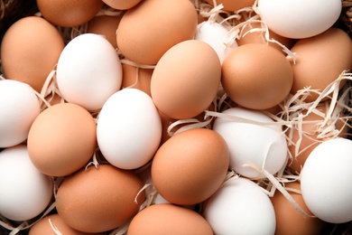 Photo of Pile of raw chicken eggs in straw, top view