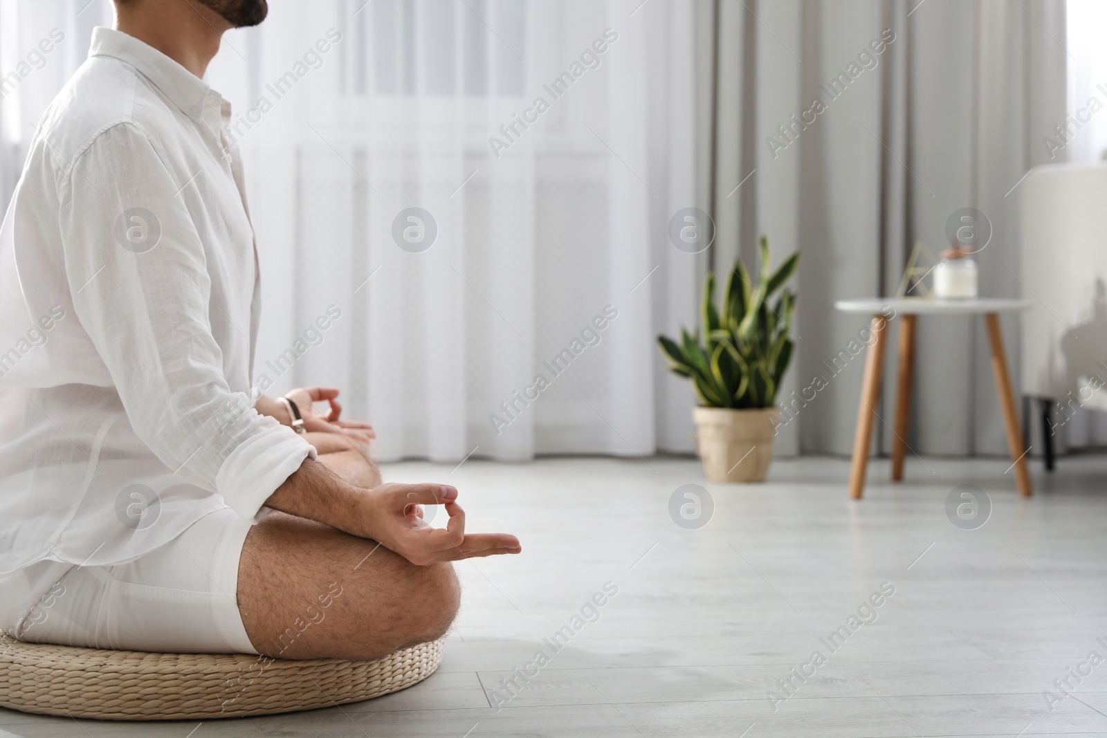 Photo of Young man meditating on straw cushion at home, closeup. Space for text