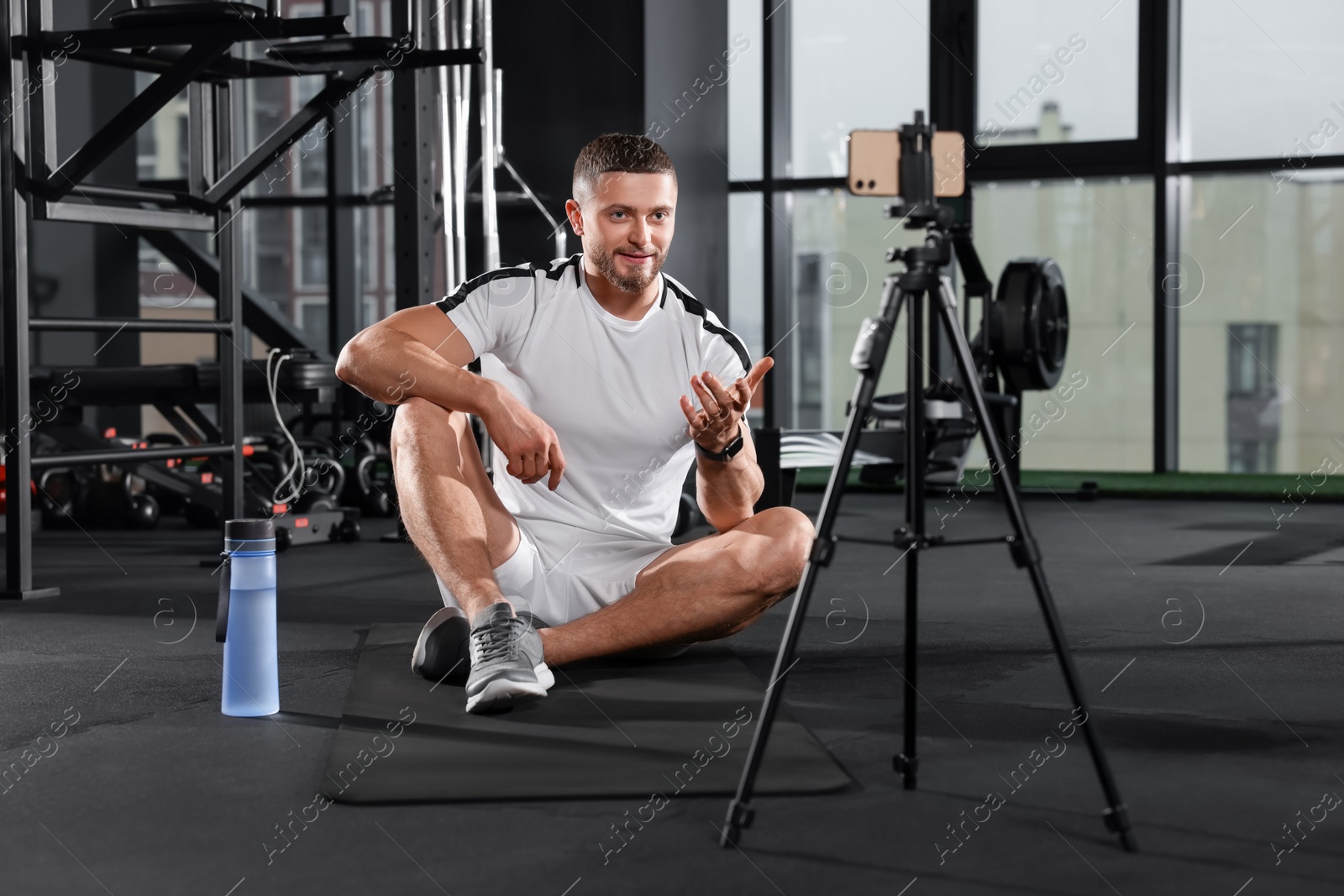 Photo of Trainer streaming online workout with phone at gym