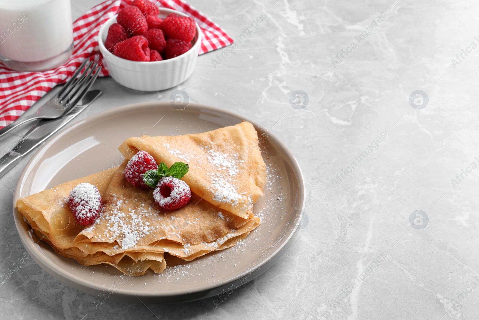 Photo of Delicious crepes served with mint, raspberries and powdered sugar on grey table. Space for text