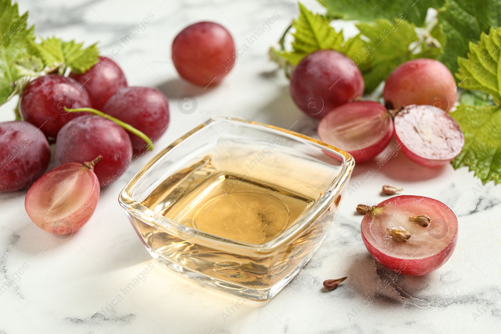 Photo of Bowl of natural grape seed oil on white marble table. Organic cosmetic