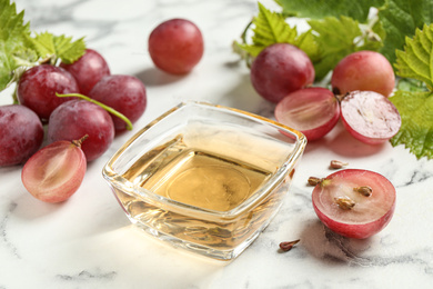 Photo of Bowl of natural grape seed oil on white marble table. Organic cosmetic